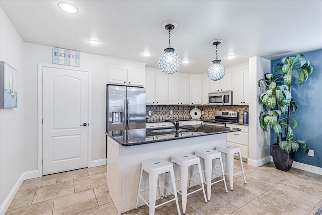 kitchen featuring backsplash, dark stone counters, an island with sink, white cabinetry, and stainless steel appliances