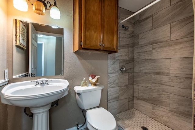 full bath featuring a tile shower, toilet, and a textured wall