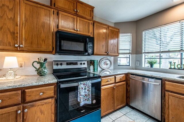 kitchen featuring tasteful backsplash, brown cabinets, light tile patterned flooring, appliances with stainless steel finishes, and light stone countertops
