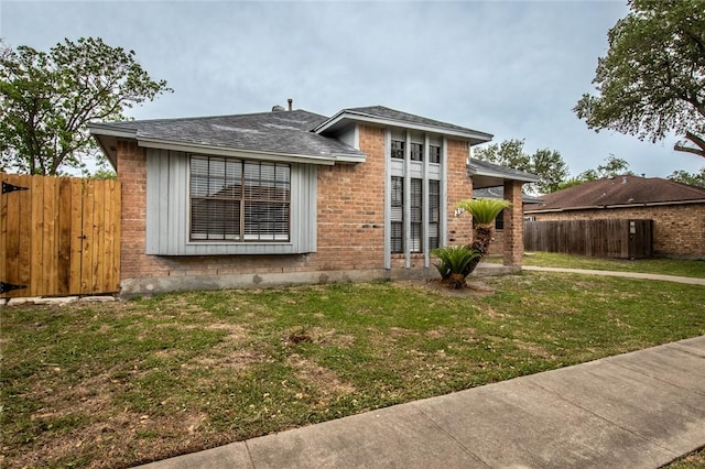 rear view of property featuring fence, a lawn, brick siding, and roof with shingles