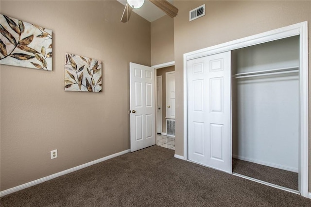 unfurnished bedroom with a closet, a towering ceiling, baseboards, carpet flooring, and visible vents