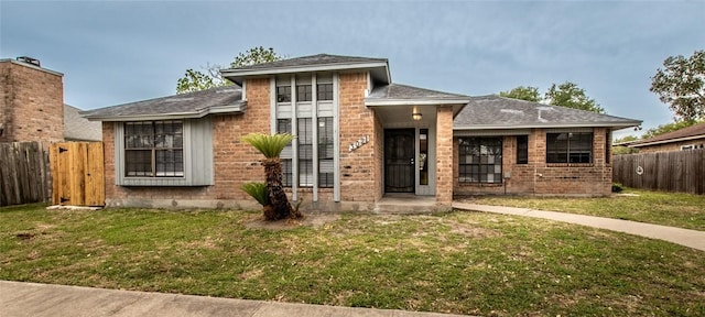 view of front of home with fence, a shingled roof, brick siding, and a front yard