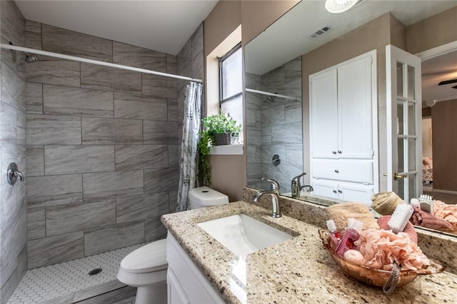 bathroom featuring a tile shower, toilet, vanity, and visible vents