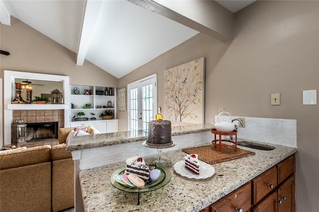 living area with ceiling fan, french doors, vaulted ceiling with beams, and a fireplace