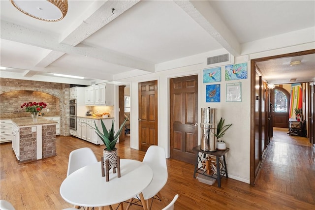 dining space with beam ceiling, wood finished floors, and visible vents