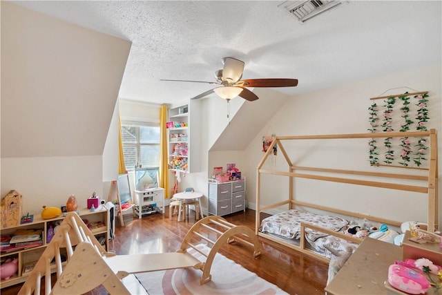 recreation room featuring a ceiling fan, wood finished floors, visible vents, lofted ceiling, and a textured ceiling