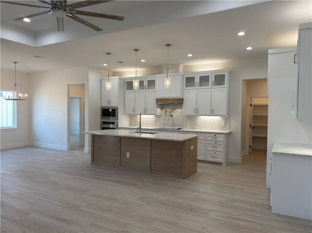 kitchen with built in microwave, a sink, decorative backsplash, oven, and ceiling fan with notable chandelier