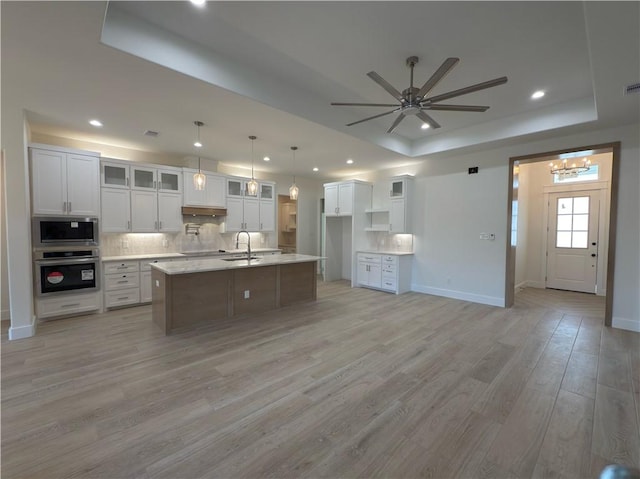 kitchen featuring light wood finished floors, a tray ceiling, decorative backsplash, stainless steel appliances, and a sink