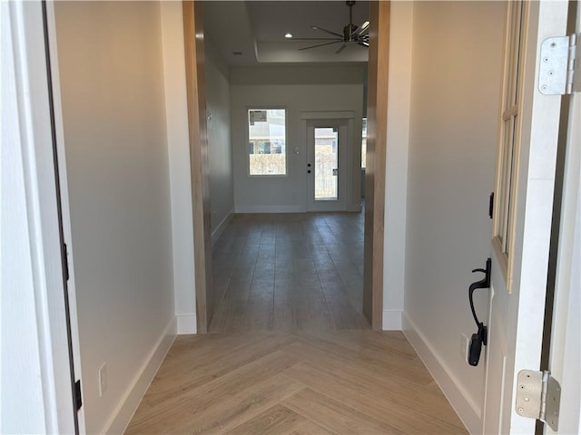 hallway with recessed lighting, a tray ceiling, baseboards, and parquet flooring