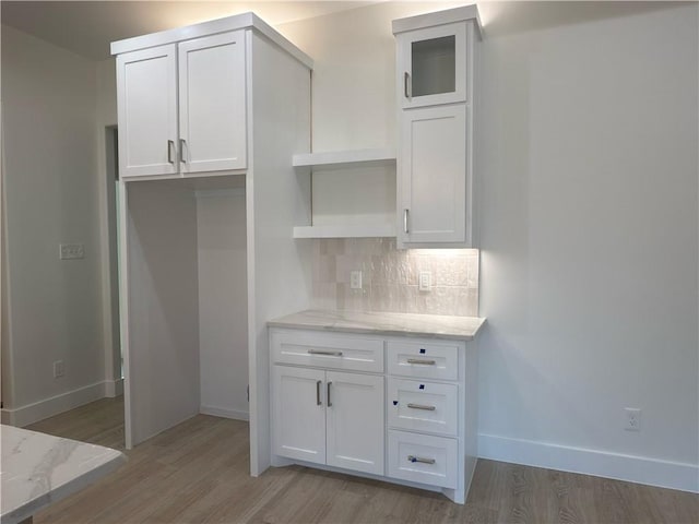 kitchen with decorative backsplash, white cabinets, light wood-style floors, and light stone countertops