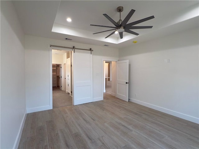 unfurnished bedroom featuring a tray ceiling, a barn door, baseboards, and light wood-style flooring