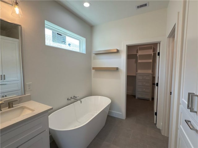 bathroom with visible vents, a walk in closet, a freestanding bath, tile patterned floors, and vanity