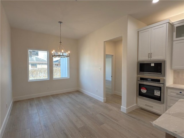 unfurnished dining area with a chandelier, light wood-type flooring, and baseboards