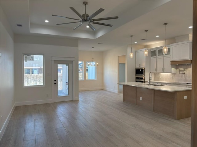 kitchen featuring visible vents, a sink, decorative backsplash, a raised ceiling, and open floor plan