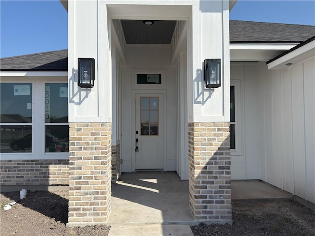 doorway to property featuring brick siding and a shingled roof