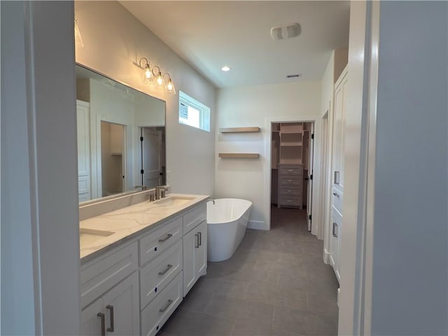 bathroom with visible vents, a walk in closet, double vanity, a freestanding tub, and a sink