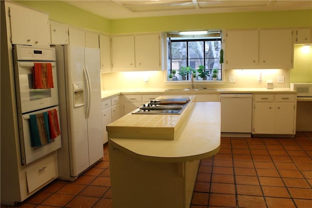 kitchen featuring white appliances, dark tile patterned floors, a sink, white cabinetry, and a center island