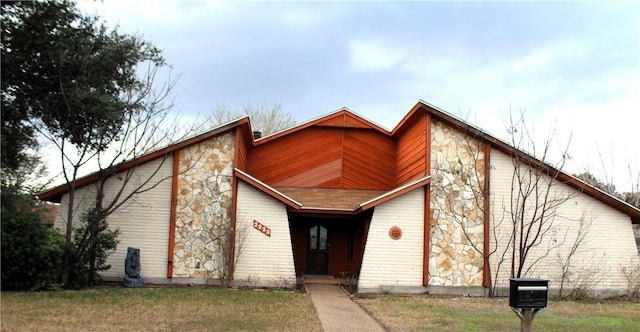 view of front of property featuring a front yard, stone siding, and brick siding