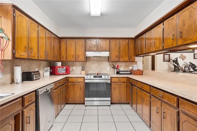 1689 Mooney Ln, Ingleside, TX 78362 - kitchen featuring stainless steel appliances, under cabinet range hood, brown cabinetry, light tile patterned floors, and light countertops