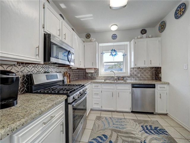 kitchen with light tile patterned floors, a sink, stainless steel appliances, white cabinetry, and backsplash