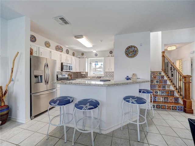 kitchen with light tile patterned floors, visible vents, appliances with stainless steel finishes, decorative backsplash, and a kitchen bar