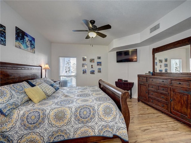 bedroom featuring ceiling fan, light wood-style flooring, a textured ceiling, and visible vents