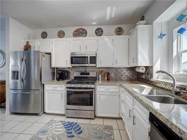 kitchen featuring light tile patterned floors, a sink, white cabinets, appliances with stainless steel finishes, and backsplash