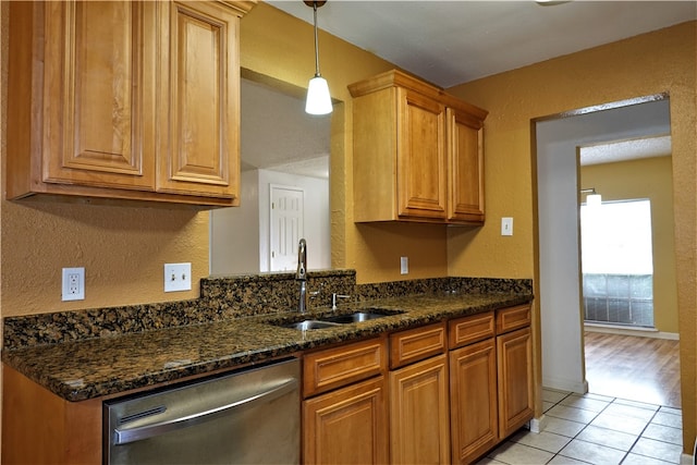 kitchen with sink, stainless steel dishwasher, dark stone countertops, decorative light fixtures, and light tile patterned flooring