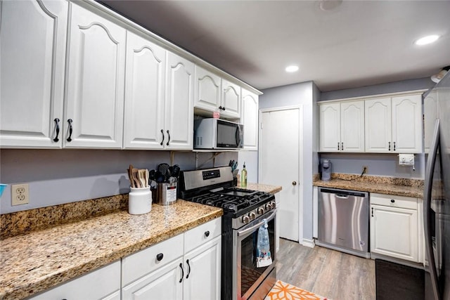 kitchen with white cabinetry, stainless steel appliances, light stone countertops, and light hardwood / wood-style flooring