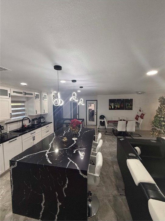 kitchen featuring a textured ceiling, sink, pendant lighting, a center island, and white cabinetry