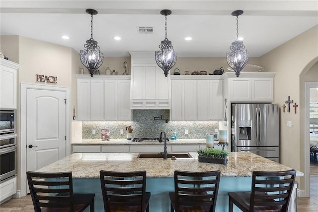 kitchen featuring visible vents, decorative backsplash, appliances with stainless steel finishes, white cabinetry, and a sink