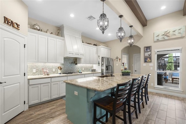 kitchen featuring visible vents, arched walkways, decorative backsplash, custom range hood, and a sink