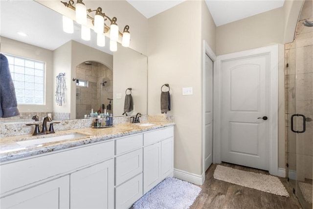 bathroom featuring double vanity, a sink, a shower stall, and wood finished floors