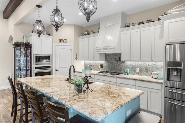 kitchen featuring a sink, white cabinets, appliances with stainless steel finishes, custom exhaust hood, and decorative backsplash