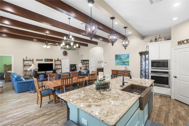 kitchen featuring arched walkways, light wood-style flooring, white cabinetry, appliances with stainless steel finishes, and decorative light fixtures