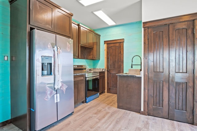 kitchen featuring light stone countertops, appliances with stainless steel finishes, wooden walls, and light hardwood / wood-style floors