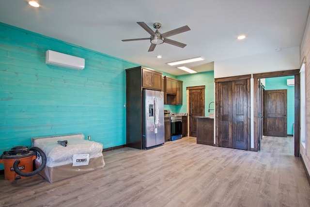 kitchen with a wall unit AC, wooden walls, ceiling fan, light wood-type flooring, and appliances with stainless steel finishes