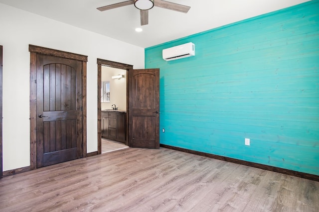 unfurnished bedroom with connected bathroom, sink, a wall mounted air conditioner, light hardwood / wood-style floors, and ceiling fan