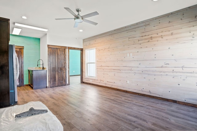 unfurnished bedroom with wooden walls, sink, ceiling fan, stainless steel refrigerator, and light hardwood / wood-style flooring