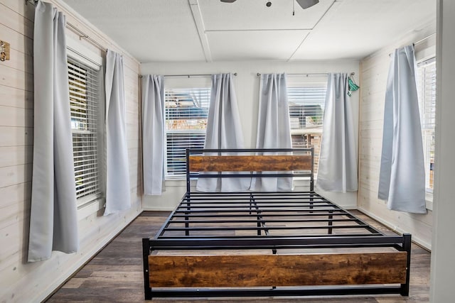 bedroom with wood walls, ceiling fan, and dark wood-type flooring