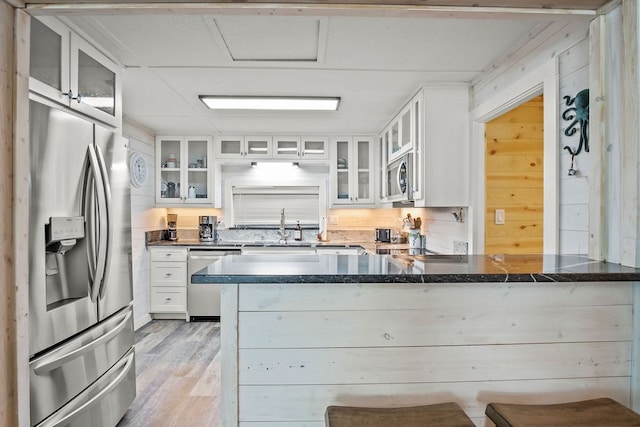 kitchen with stainless steel appliances, light hardwood / wood-style floors, kitchen peninsula, a breakfast bar area, and white cabinetry