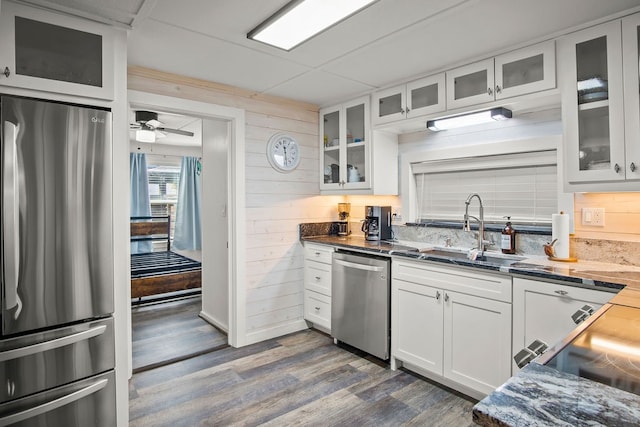 kitchen with white cabinetry, appliances with stainless steel finishes, dark hardwood / wood-style flooring, wood walls, and sink