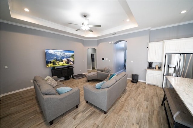 living room with a tray ceiling, light hardwood / wood-style flooring, ornamental molding, and ceiling fan