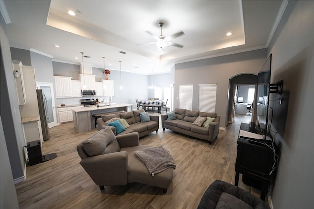 living room featuring ceiling fan, a tray ceiling, sink, and light hardwood / wood-style flooring