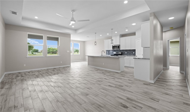 kitchen with a kitchen island with sink, a tray ceiling, decorative light fixtures, white cabinetry, and stainless steel appliances