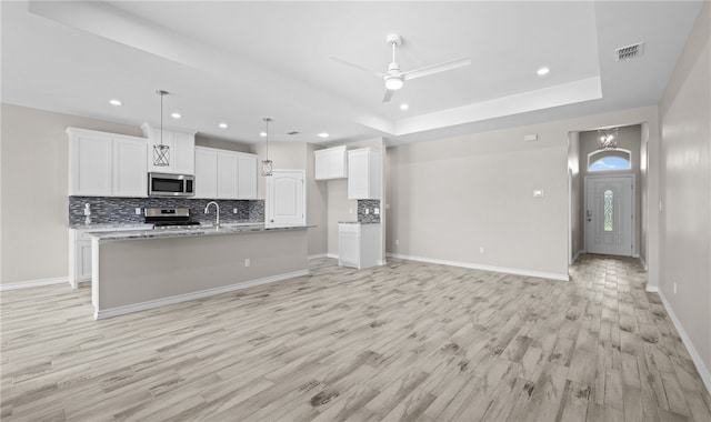 kitchen featuring a center island with sink, a tray ceiling, decorative light fixtures, white cabinetry, and stainless steel appliances