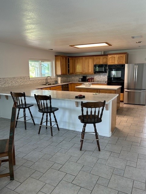 kitchen featuring sink, stainless steel fridge, a breakfast bar area, tasteful backsplash, and kitchen peninsula