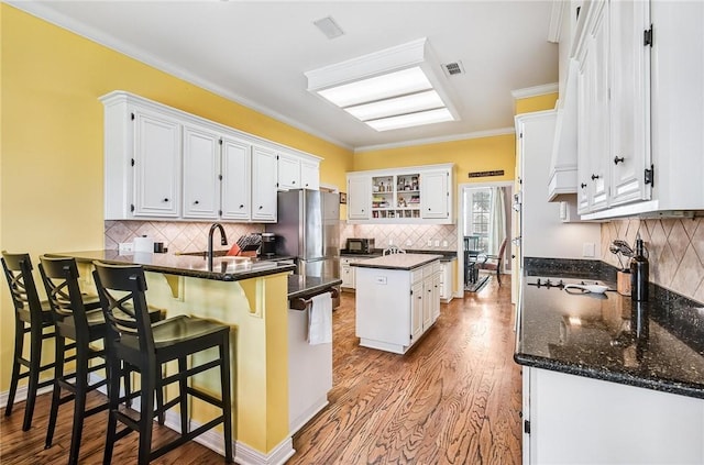 5918 Woodmere Dr, Corpus Christi, TX 78414 - kitchen with a peninsula, freestanding refrigerator, decorative backsplash, white cabinets, and light wood-type flooring