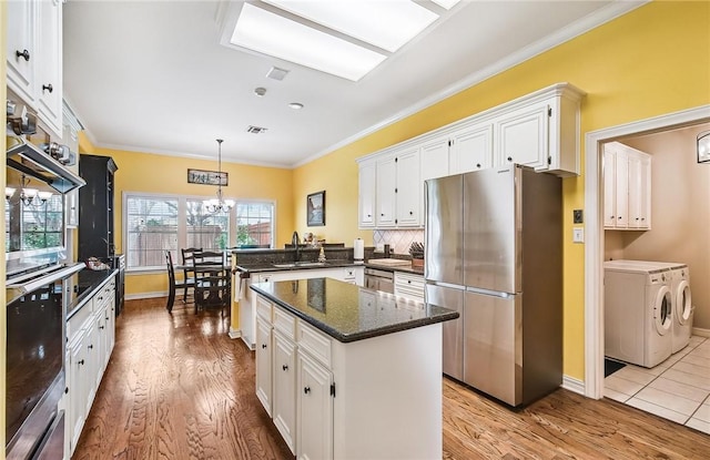 5918 Woodmere Dr, Corpus Christi, TX 78414 - kitchen featuring appliances with stainless steel finishes, washing machine and clothes dryer, a peninsula, white cabinetry, and wood finished floors