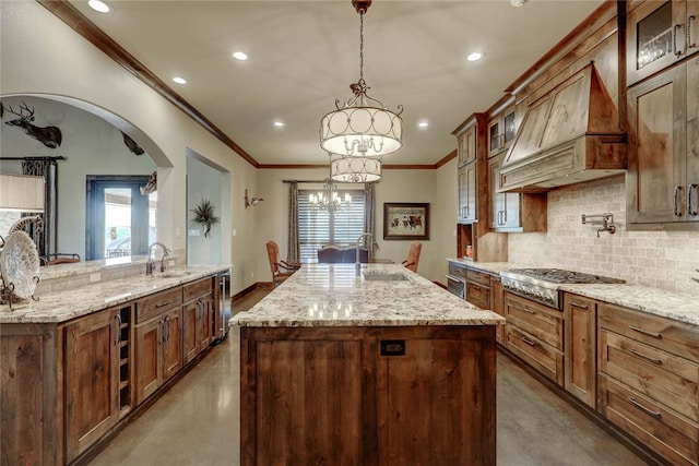 kitchen with sink, an island with sink, decorative light fixtures, stainless steel gas stovetop, and custom range hood